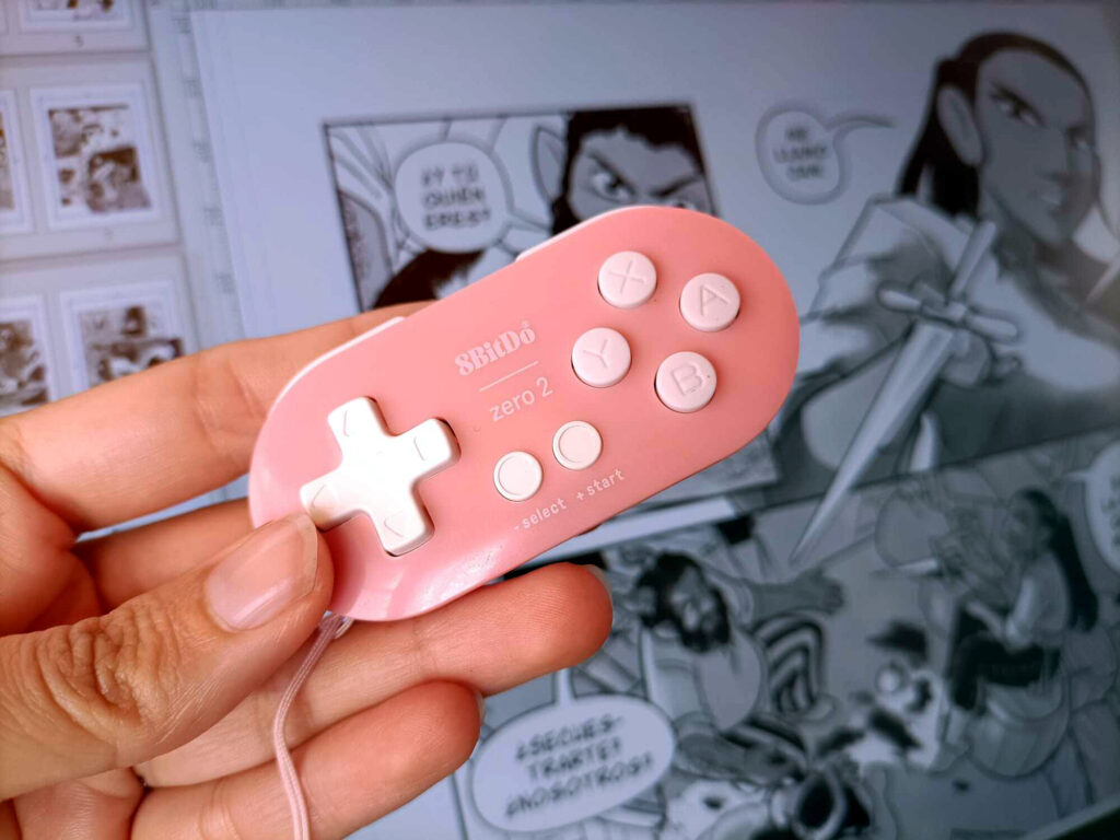 Foto de una mano delante de una tableta gráfica, sosteniendo un mando 8bitdo rosa