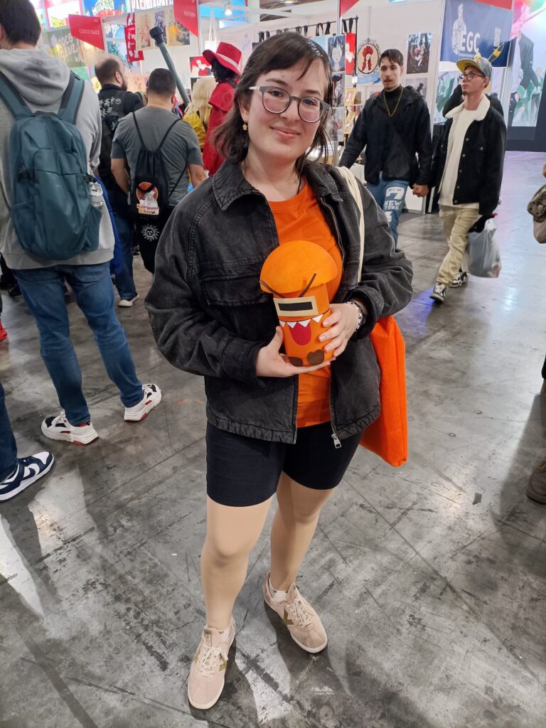 Foto de un pasillo del salón del manga. En el centro está una chica cosplayeada de Gala, el personaje de Villacolmillo, sosteniendo un Mimencio chiquitito