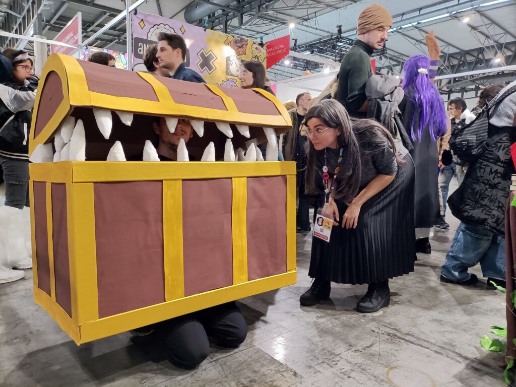 Foto de Laurielle con falda negra y agachada mirando un cosplay de un señor arrodillado en el suelo vestido de cofre entreabierto con dientes 