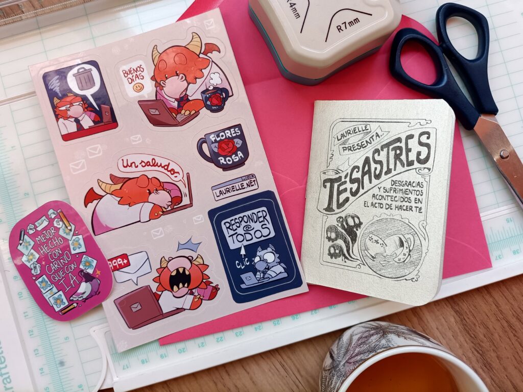 Bodegón con las distintas recompensas de la carta de tacitas de primavera 2026 (pegatina, hoja de pegatinas y minicómic) puestas sobre una superficie plana, con materiales de papelería y té