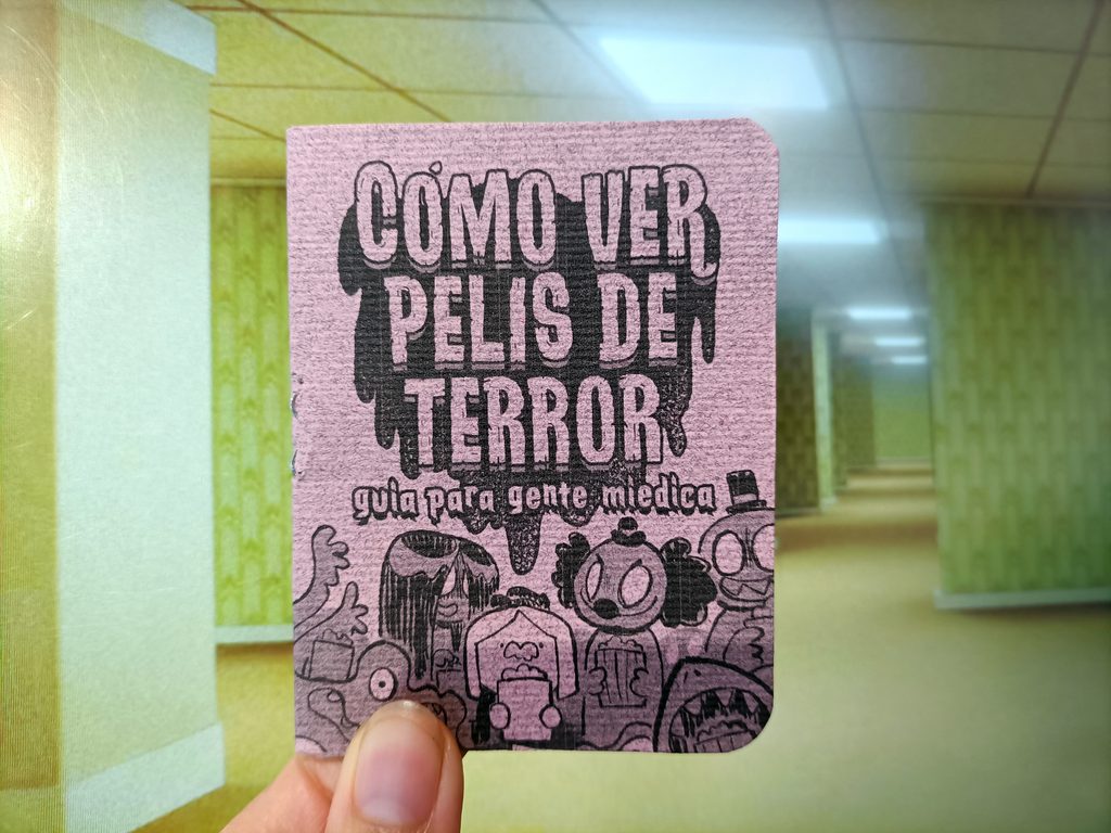 Foto de un minizine de cómo ver pelis de terror sostenido sobre un fondo de The backrooms